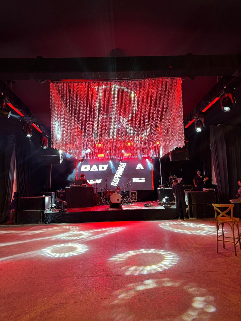Palco para banda com cortina de cristais cintilantes e iluminação de show em tons de vermelho.