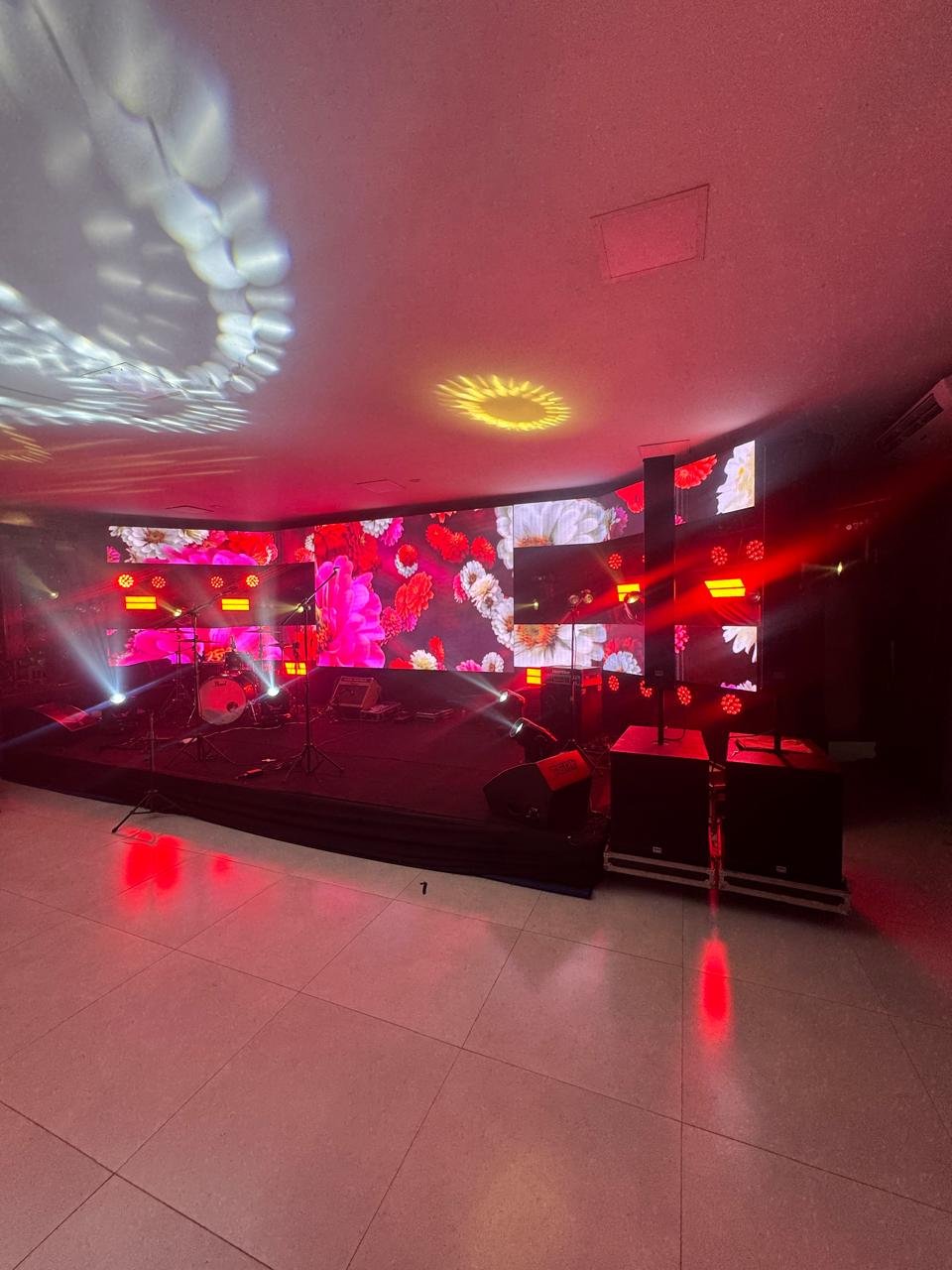 Palco com configuração para banda, iluminação vermelha e painel de LED com fundo floral.