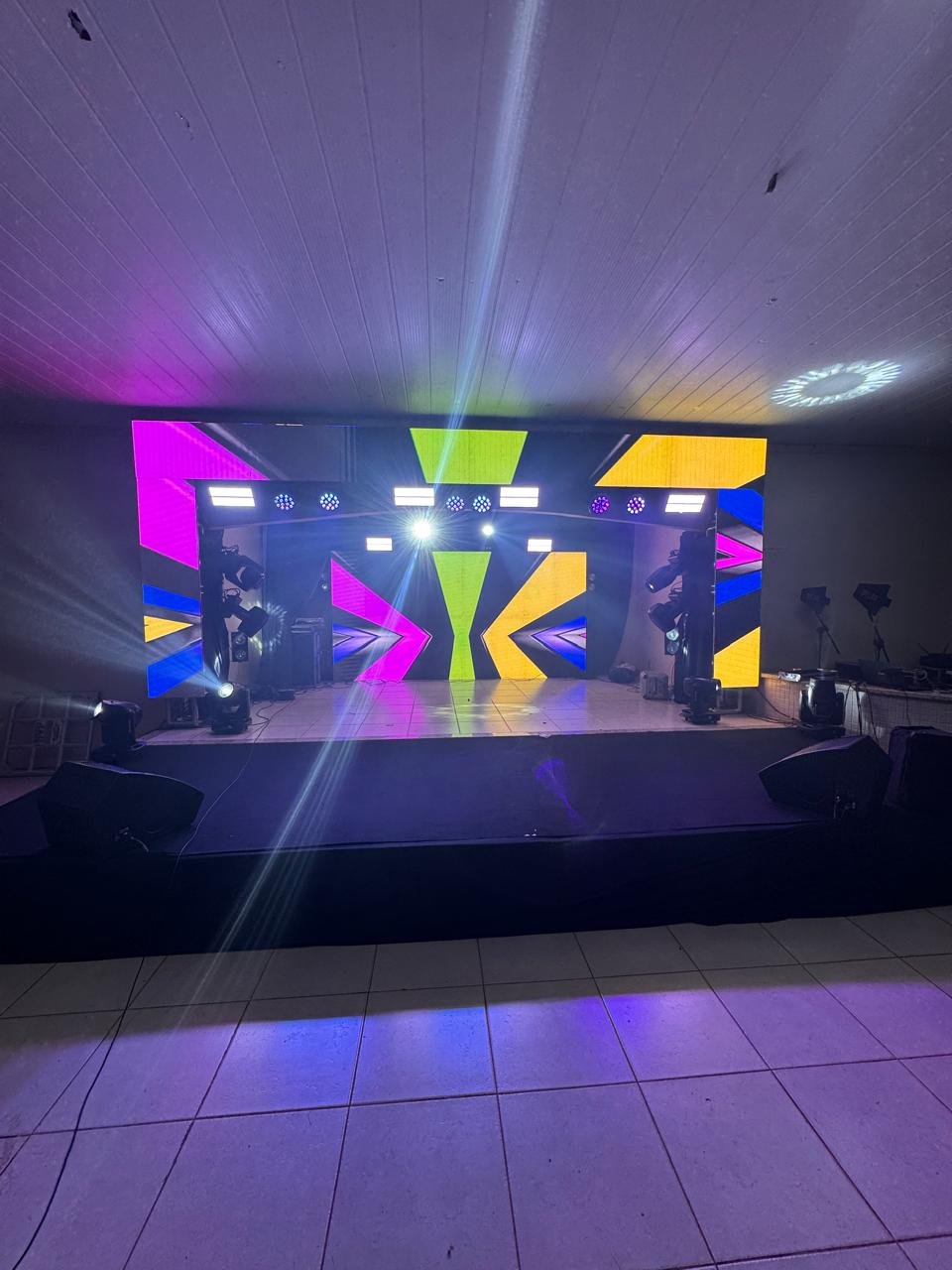 Palco moderno com painel de LED geométrico vibrante (neon) e estrutura de iluminação com moving heads.