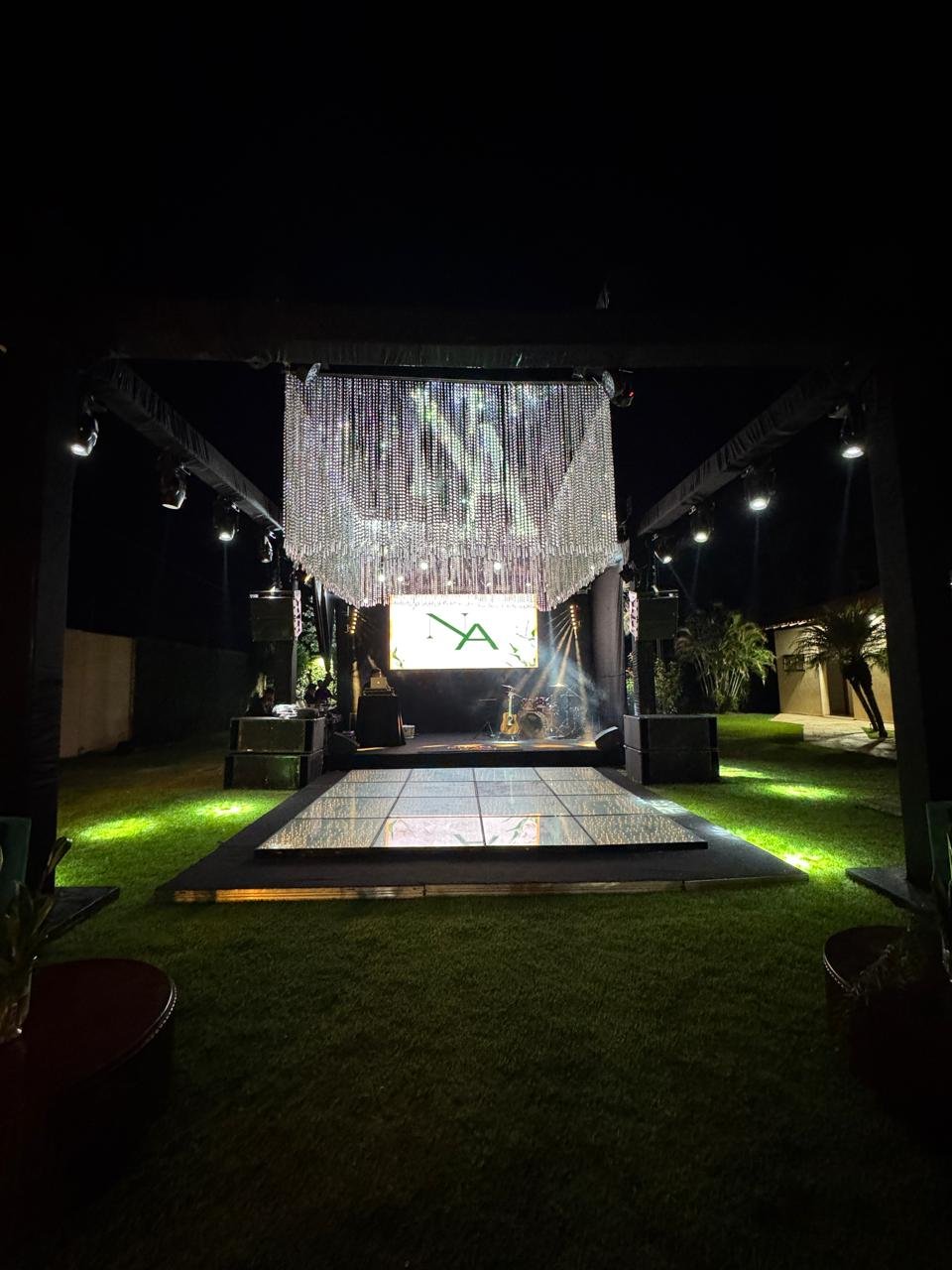 Estrutura de palco e pista de dança montada em área externa gramada, com cortina de cristais e iluminação noturna.