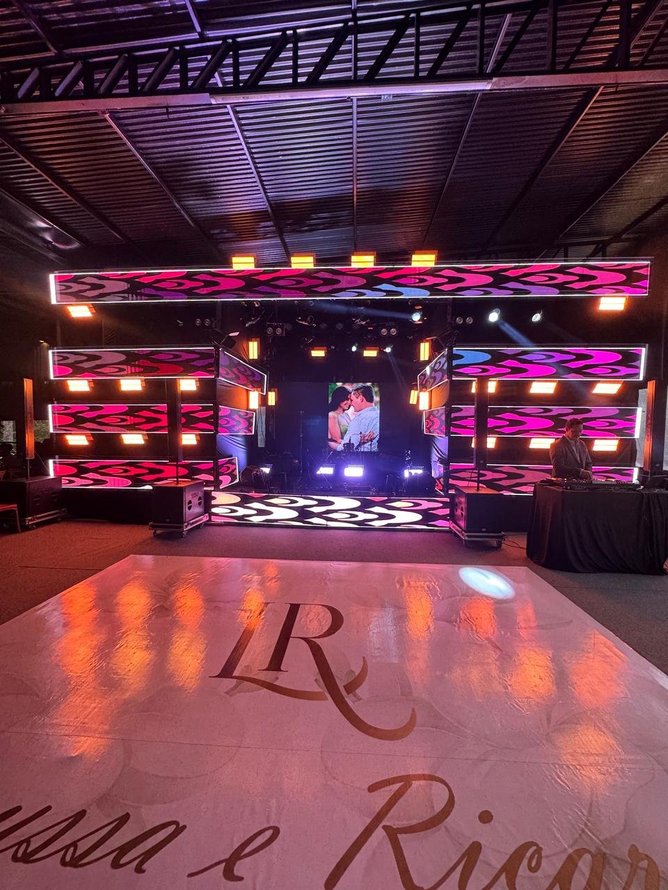 Estrutura de palco para casamento com painéis de LED modernos, iluminação cênica e pista de dança personalizada com monograma dos noivos.